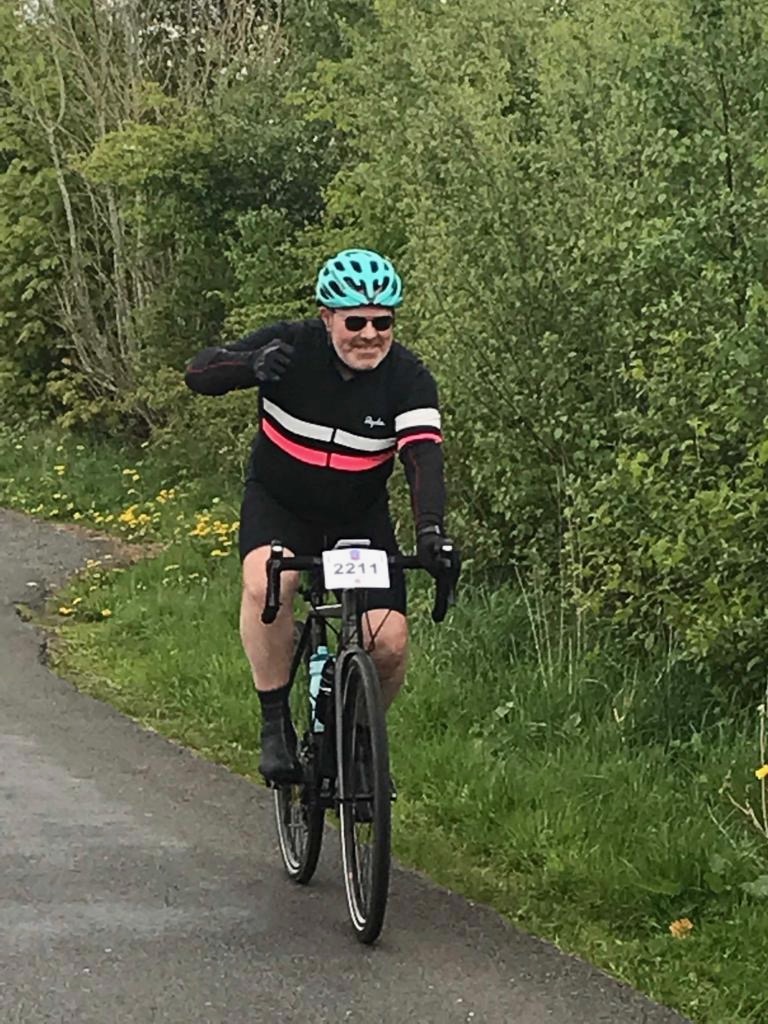 The author  wearing Rapha gear on his Cannondale CAADX cyclocross bike in a lane near Keswick in the Lake District, England, UK. The author rides triumphantly with his right hand pumping the air. 