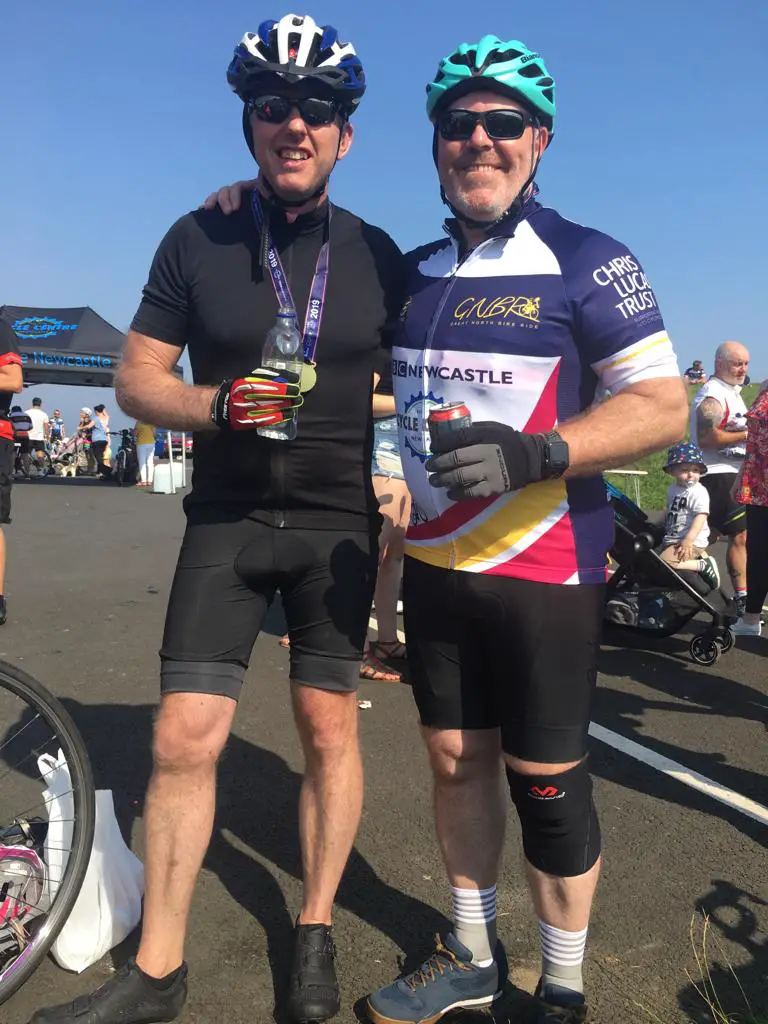 two men in cycling gear enjoying a drink 