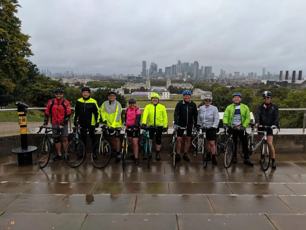 Goup of cyclists posing for a photo in the rain with London in the background
