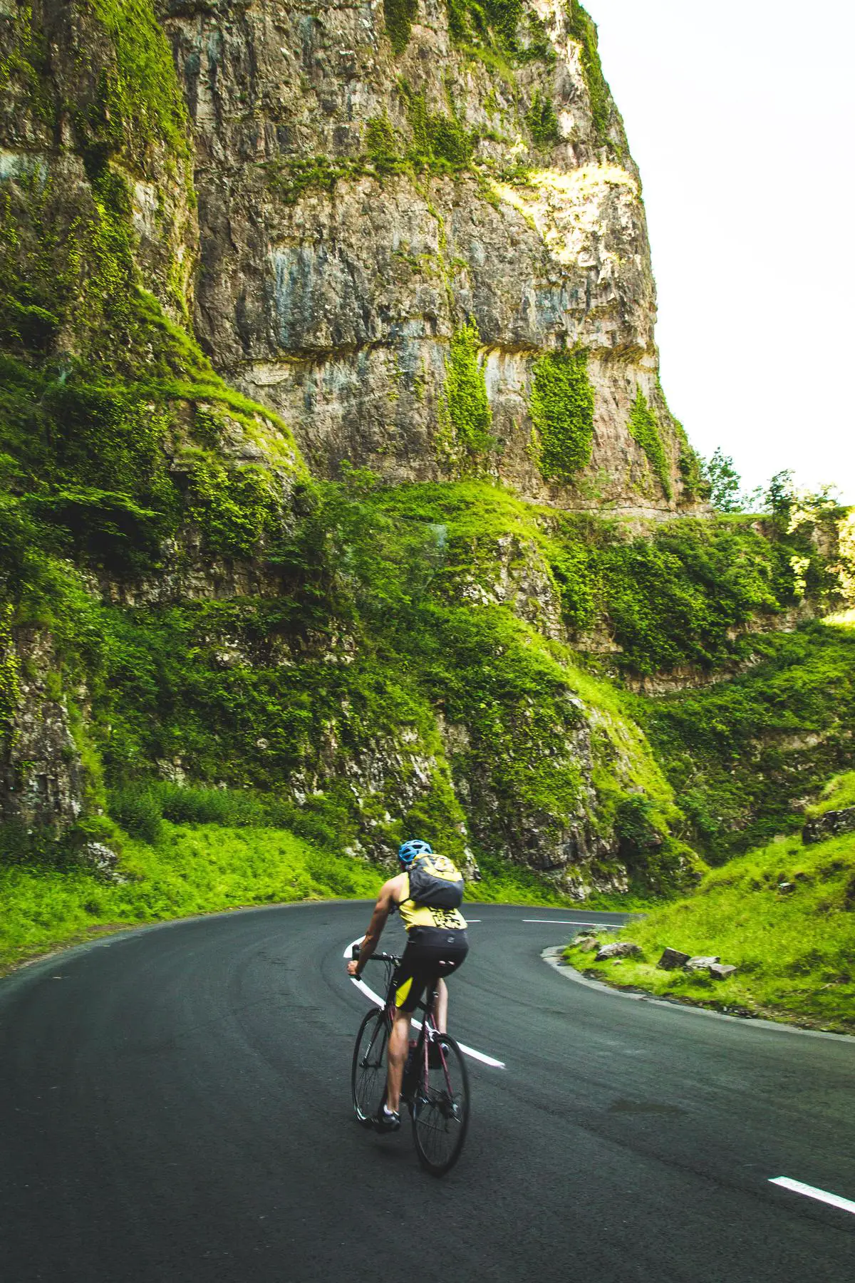 A person on a bike with a worried look on their face, looking up towards a steep hill and the open sky above.